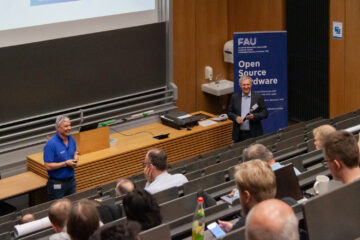 Zwei Personen halten einen Vortrag vor vielen Menschen
