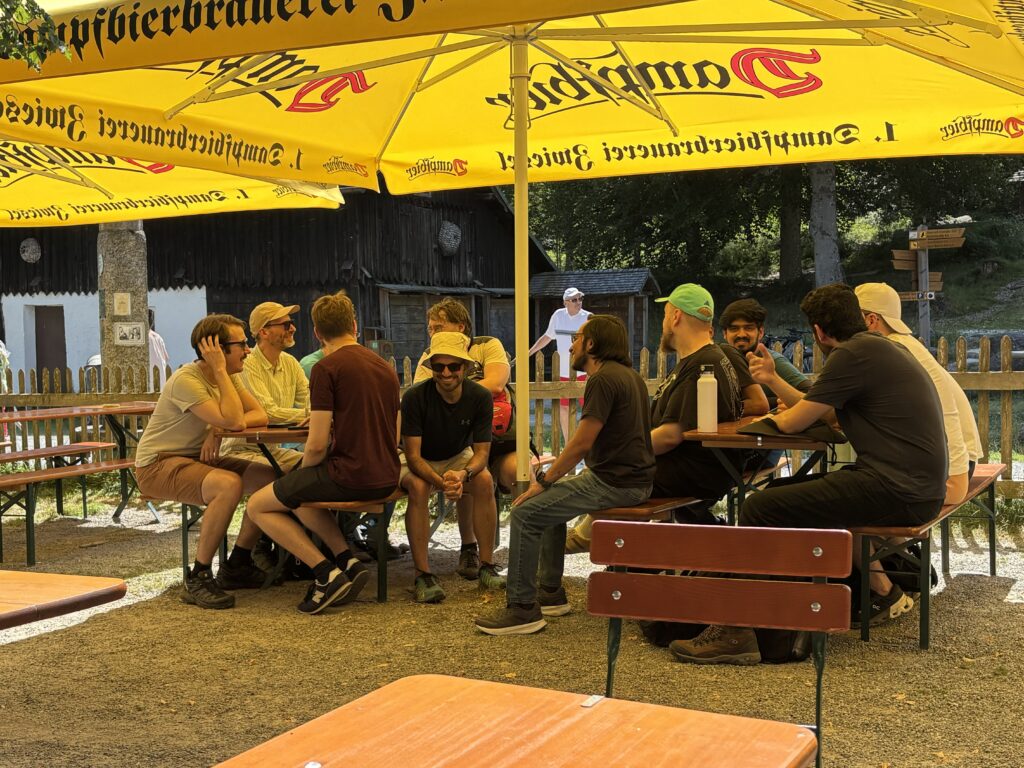 Eine Gruppe von Personen sitzt auf Bierbänken im Schatten